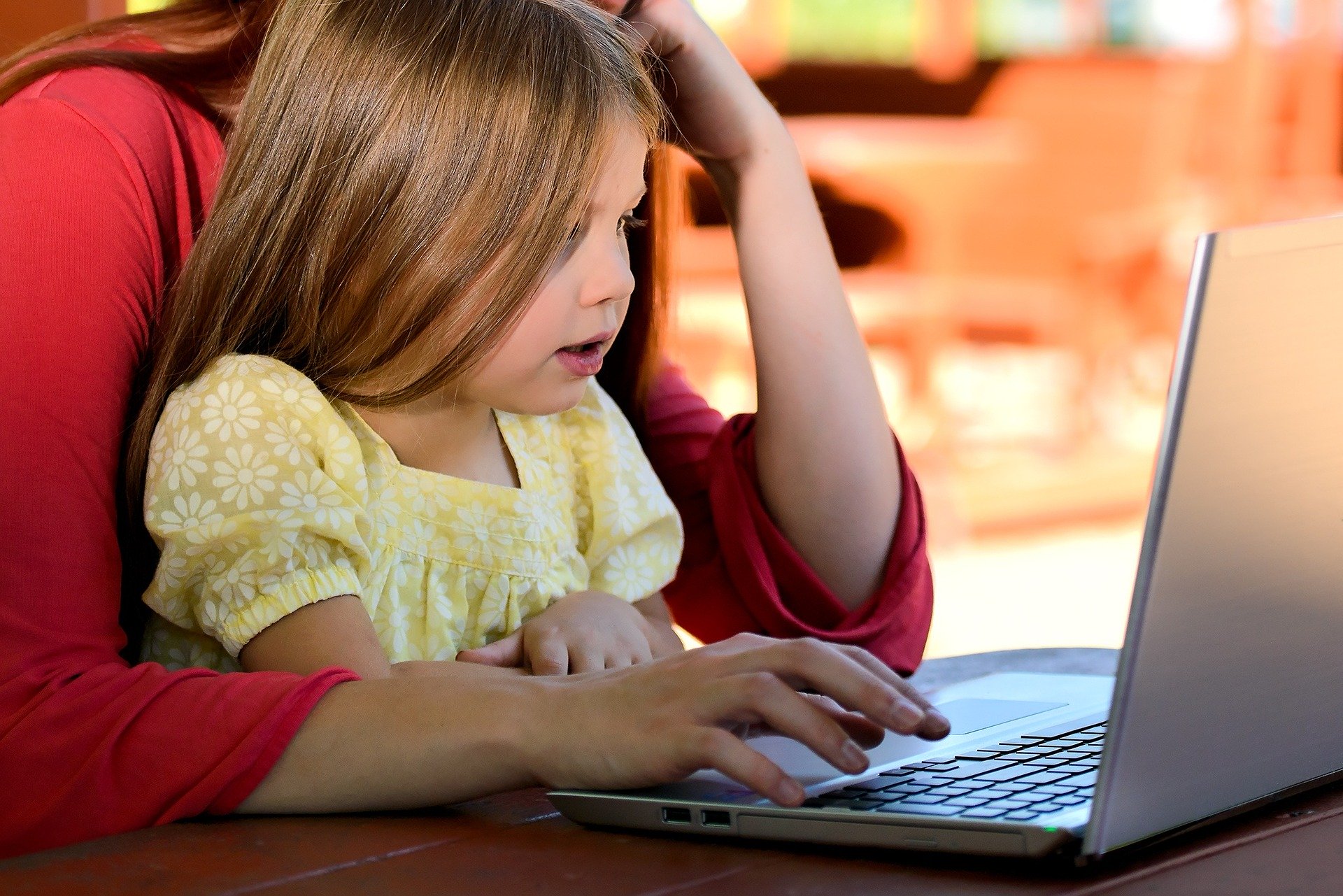 Young girl (with her mother, who is out of view) looking at a screen of a laptop